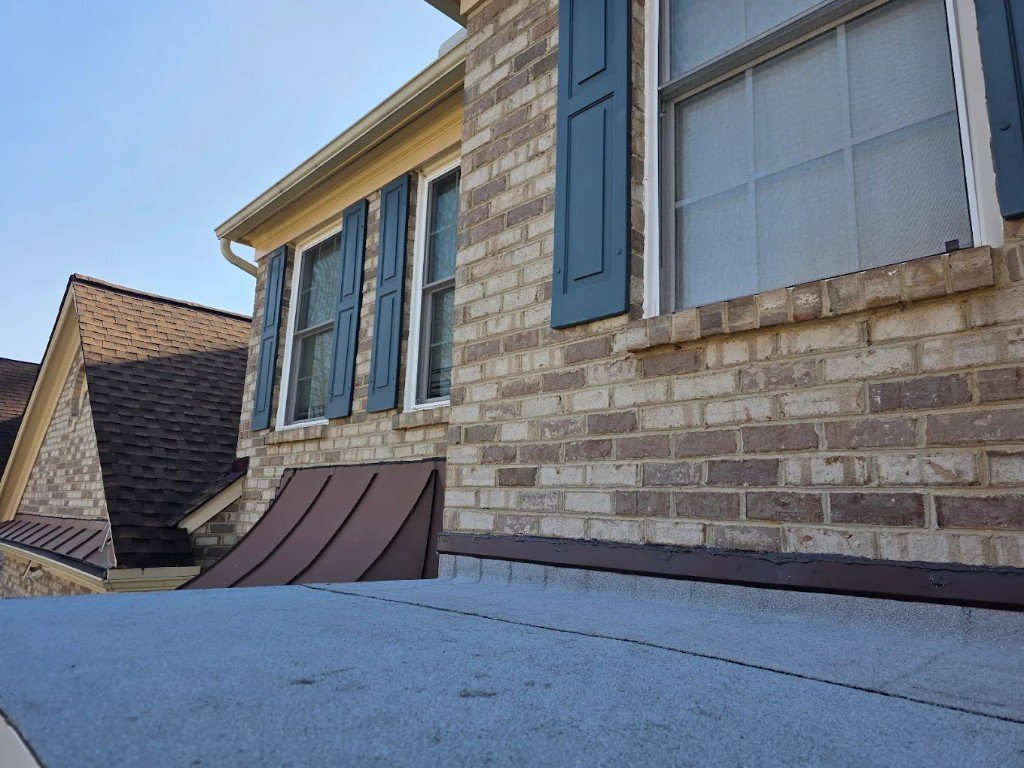 Low-slope roof detail against a brick home with standing-seam accent roof