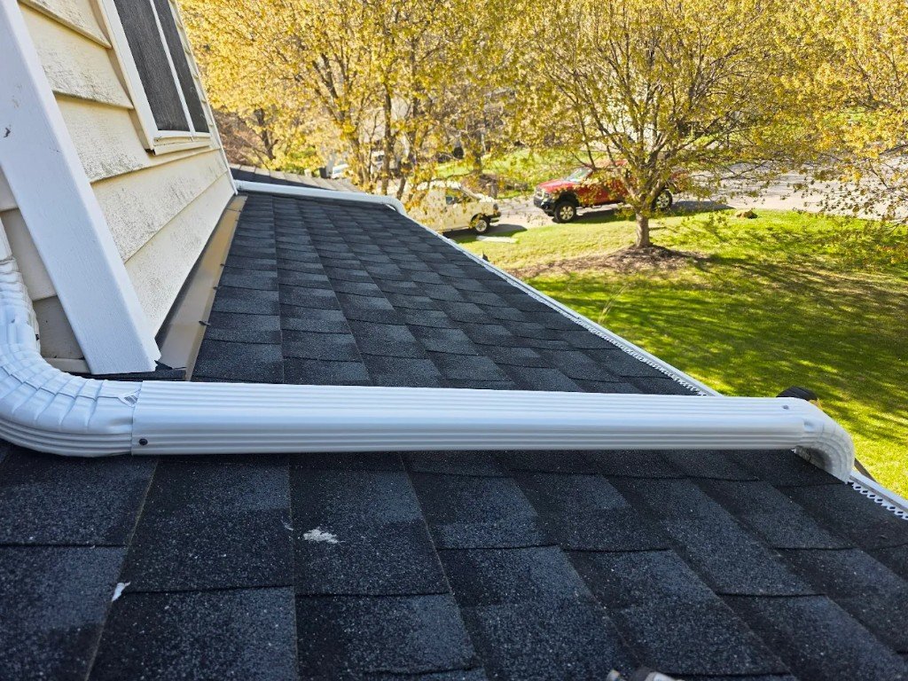Seamless gutter and downspout installed along a shingle roof edge