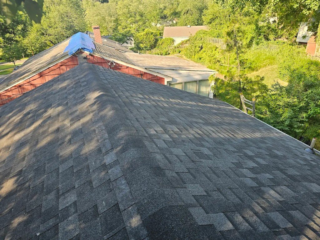 Shingle roof ridge line installation over a wooded backyard